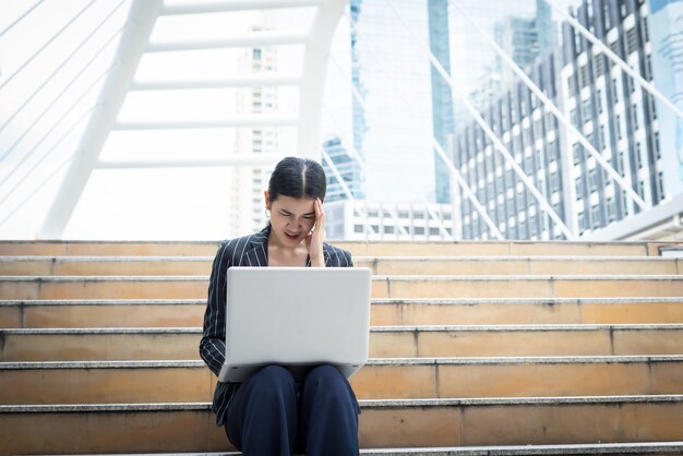 Donna di affari ha sottolineato mentre usando il computer portatile si siede sui gradini. Concetto di persone d&#39;affari.