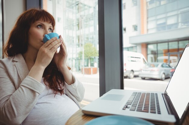 Donna di affari incinta che mangia caffè nella caffetteria