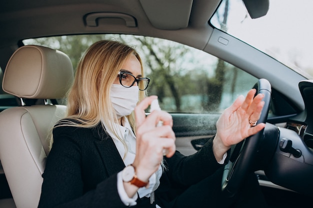 Donna di affari nella maschera di protezione che si siede dentro un'automobile facendo uso dell'antisettico