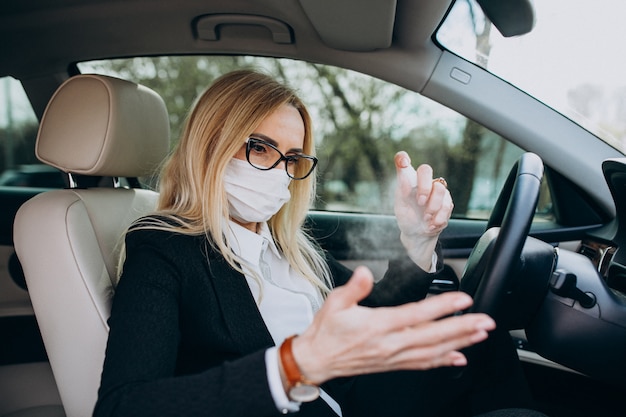 Donna di affari nella maschera di protezione che si siede dentro un'automobile facendo uso dell'antisettico