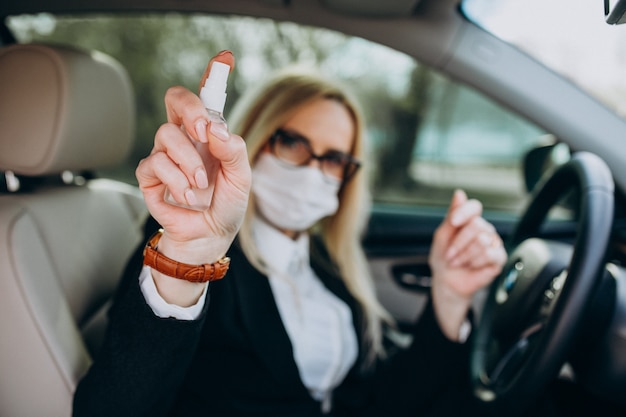 Donna di affari nella maschera di protezione che si siede dentro un'automobile facendo uso dell'antisettico