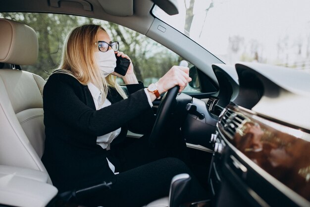 Donna di affari nella maschera di protezione che si siede dentro un'automobile