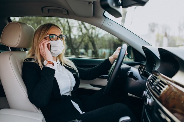 Donna di affari nella maschera di protezione che si siede dentro un'automobile