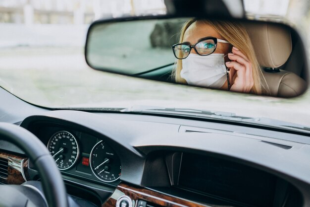 Donna di affari nella maschera di protezione che si siede dentro un'automobile