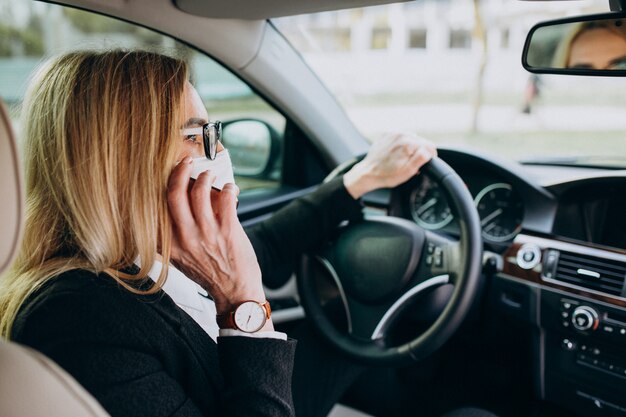 Donna di affari nella maschera di protezione che si siede dentro un'automobile