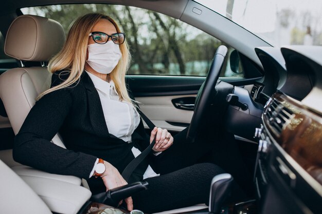 Donna di affari nella maschera di protezione che si siede dentro un'automobile