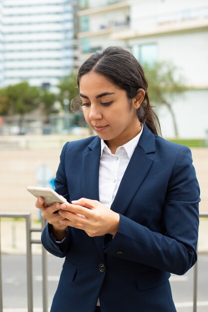 Donna di affari sorridente che per mezzo dello smartphone