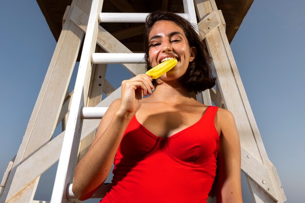 Donna di angolo basso che mangia il gelato sulla spiaggia