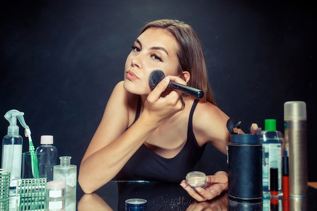 Donna di bellezza che applica trucco. Bella ragazza guardarsi allo specchio e applicare cosmetici con un pennello grande.