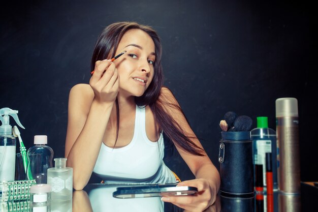 Donna di bellezza che applica trucco. Bella ragazza guardarsi allo specchio e applicare cosmetici con un pennello.