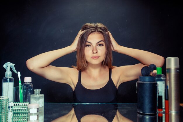 Donna di bellezza dopo aver applicato il trucco. Bella ragazza guardarsi allo specchio e applicare cosmetici con un pennello.