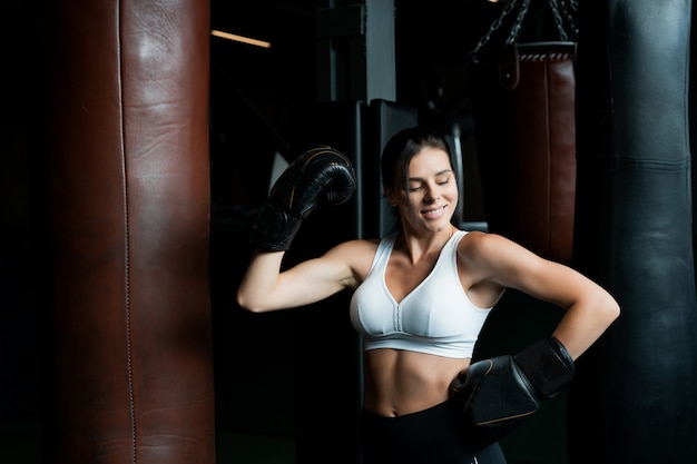 Donna di boxe in posa con il sacco da boxe, sul buio. Concetto di donna forte e indipendente