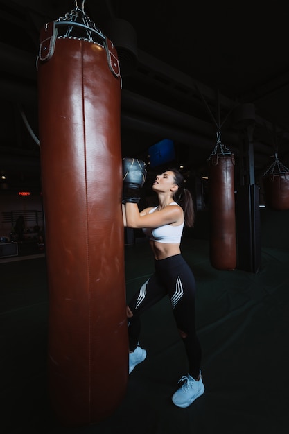 Donna di boxe in posa con il sacco da boxe, sul buio. Concetto di donna forte e indipendente