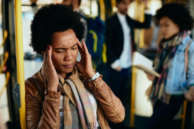 Donna di colore che si tiene la testa dolorante mentre viaggia con i mezzi pubblici