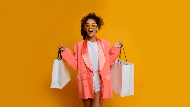 Donna di colore uscita con il sacchetto della spesa bianco che controlla fondo giallo. Look alla moda primaverile alla moda.