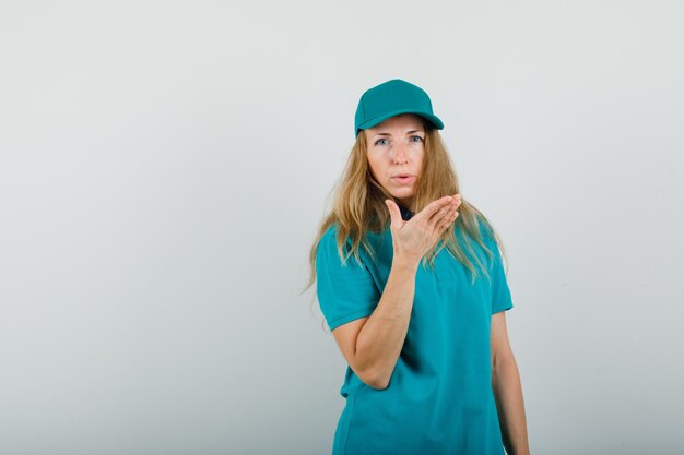 Donna di consegna che guarda l'obbiettivo con la mano alzata in t-shirt, berretto e sembra ragionevole