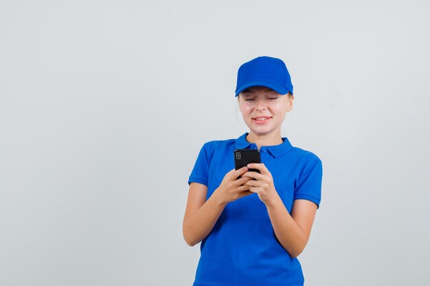 Donna di consegna che ha chat di testo sul cellulare in maglietta blu e berretto e sembra allegra
