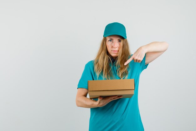 Donna di consegna che indica alla scatola di cartone in t-shirt, berretto