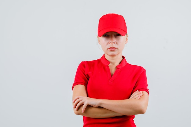 Donna di consegna in piedi con le braccia incrociate in maglietta rossa e cappello e che sembra rigorosa