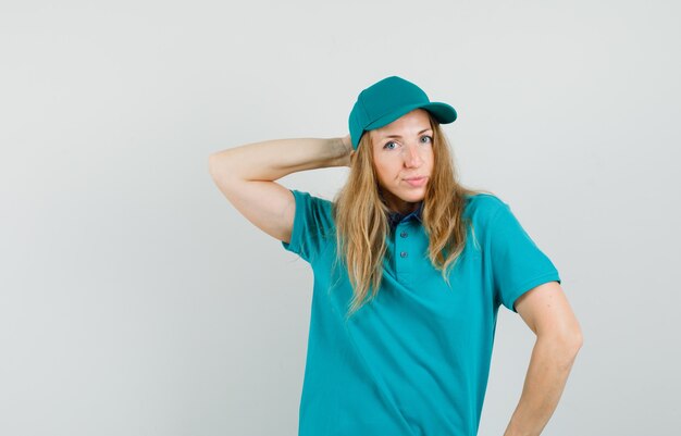 Donna di consegna in posa tenendo la mano dietro la testa in t-shirt, berretto e sembra elegante