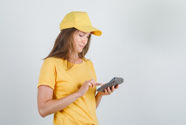 Donna di consegna in t-shirt, berretto utilizzando la calcolatrice e guardando occupato