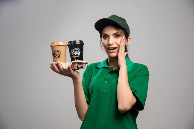 Donna di consegna in uniforme verde in piedi con tazze di caffè.