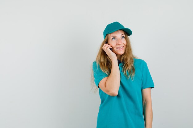 Donna di consegna parlando al cellulare in t-shirt, berretto e guardando gioiosa