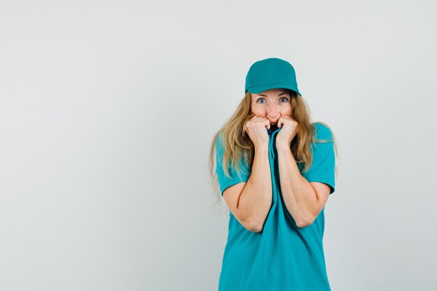 Donna di consegna tirando il colletto sul viso in t-shirt, berretto e guardando spaventato