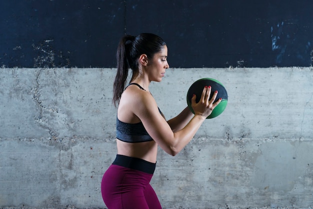 Donna di forma fisica che tiene palla medica e che si esercita in palestra