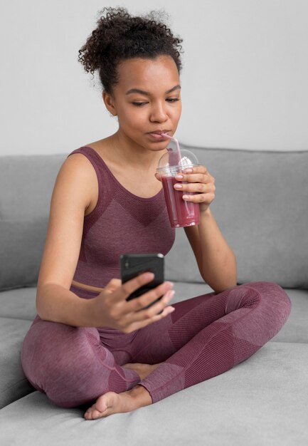 Donna di forma fisica con un succo di disintossicazione durante l'utilizzo di uno smartphone