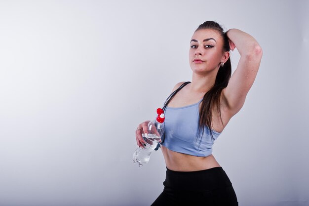 Donna di forma fisica giovane allegra bagnata in leggings superiori e neri con corda per saltare e bottiglia d'acqua isolate su sfondo bianco