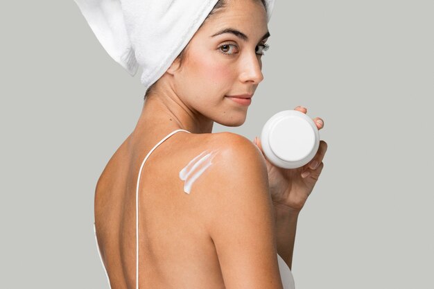 Donna di lato che tiene la crema e con un asciugamano sulla testa