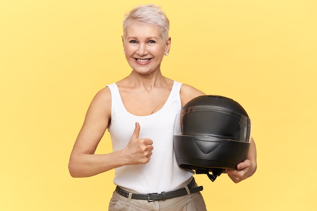 donna di mezza età atletica con capelli biondi che tiene il casco protettivo del motociclo