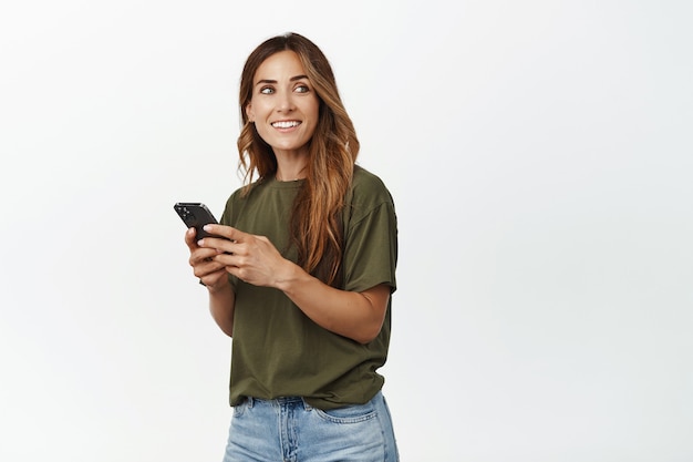 Donna di mezza età in chat, invio di messaggi di testo tramite smartphone, guardando da parte con una faccia sorridente felice