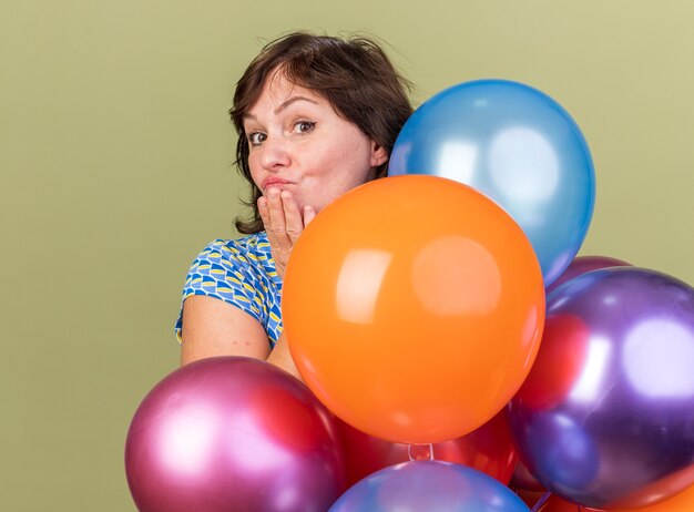 Donna di mezza età mazzo di palloncini colorati con un sorriso sulla faccia felice