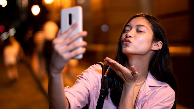 Donna di notte nelle luci della città che prende selfie e manda un bacio