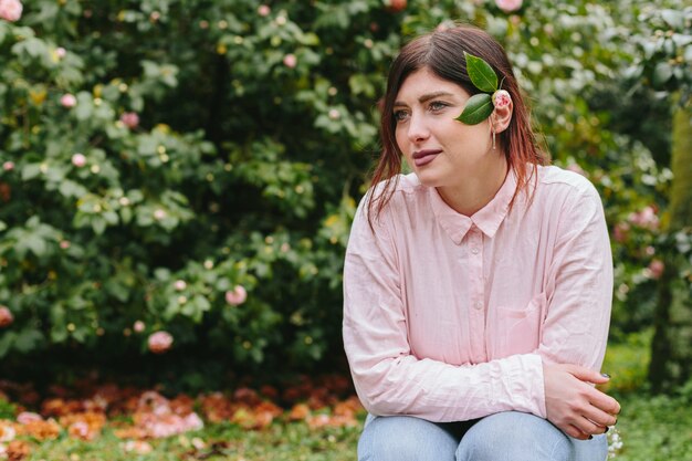 Donna di pensiero con la pianta nei capelli vicino ai fiori rosa che crescono sui ramoscelli verdi