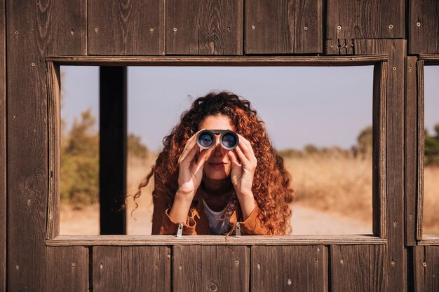 Donna di redhead di vista frontale che osserva tramite il binocolo