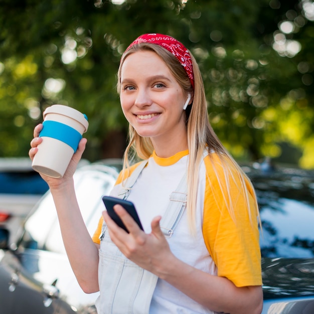 Donna di smiley all'aperto con la tazza e lo smartphone