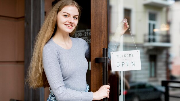 Donna di smiley che mette su segno aperto sulla porta della caffetteria