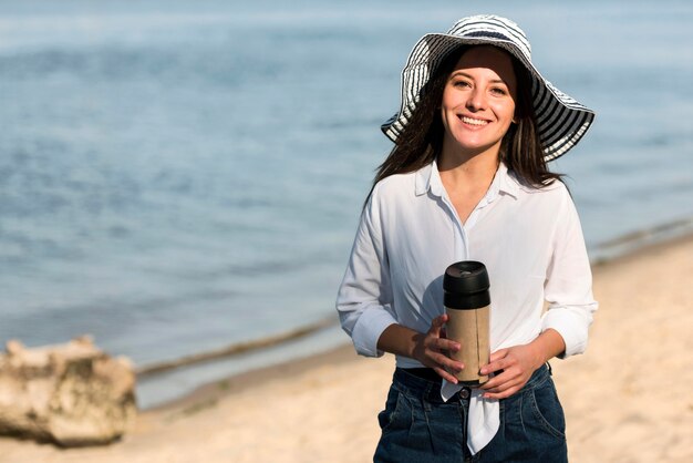 Donna di smiley che posa con il thermos sulla spiaggia