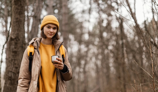 Donna di smiley che tiene tazza nella foresta