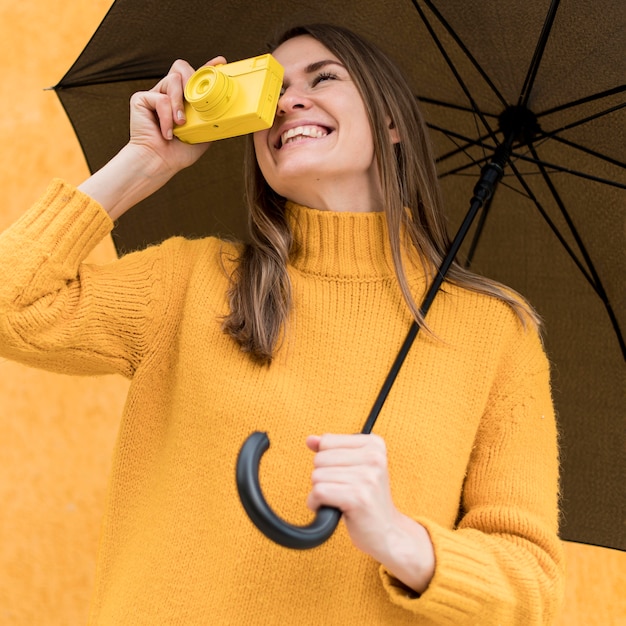 Donna di smiley che tiene un ombrello nero e una macchina fotografica gialla