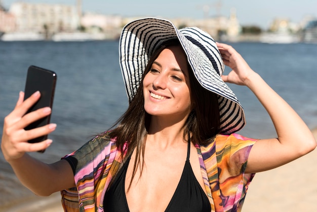 Donna di smiley con il cappello che cattura selfie in spiaggia