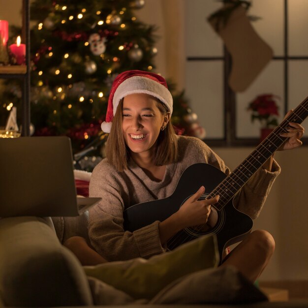 Donna di smiley con il cappello della Santa che gioca chitarra davanti al computer portatile