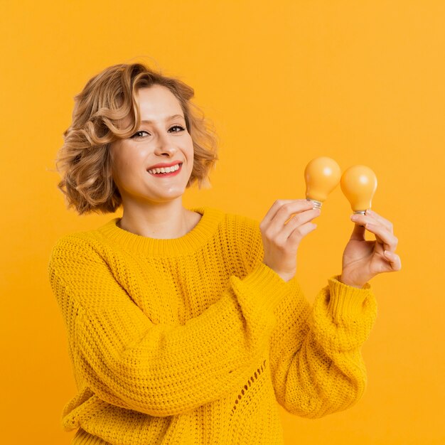 Donna di smiley dell'angolo alto che tiene le lampadine gialle