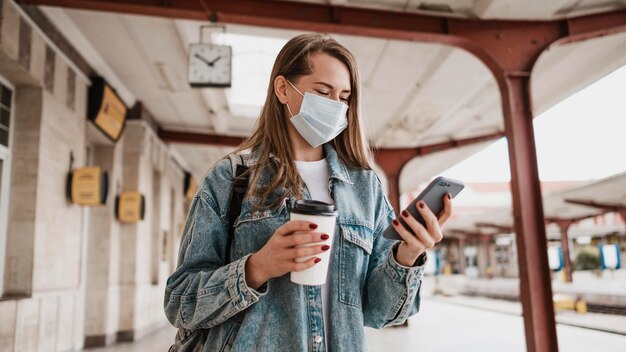 Donna di vista frontale che controlla il suo telefono cellulare alla stazione ferroviaria