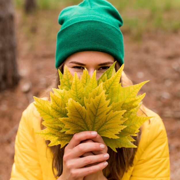 Donna di vista frontale che copre il viso con un mazzo di foglie di autunno