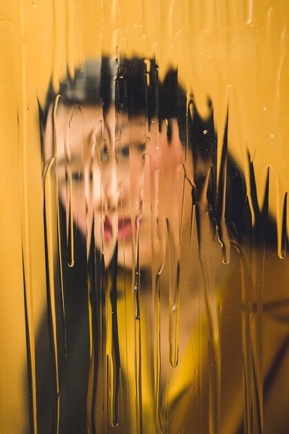 Donna di vista frontale che esamina la macchina fotografica dietro la finestra bagnata