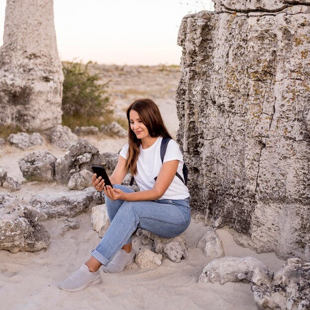 Donna di vista frontale che osserva sul suo telefono mentre era seduto su una roccia